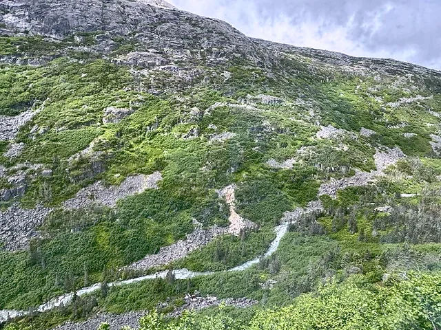 A green Alaskan ridge with walking trails below a granite summit