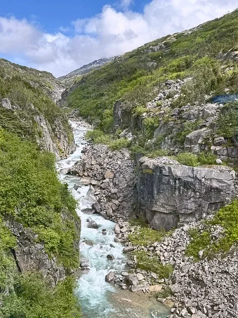 A meltwater stream running through rock and green mountainside in Alaska